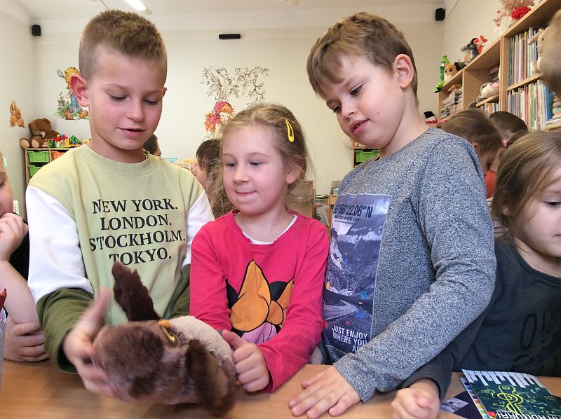 Zdjęcie przedstawia troje dzieci na zajęciach w bibliotece, które bawią się pacynką sową.