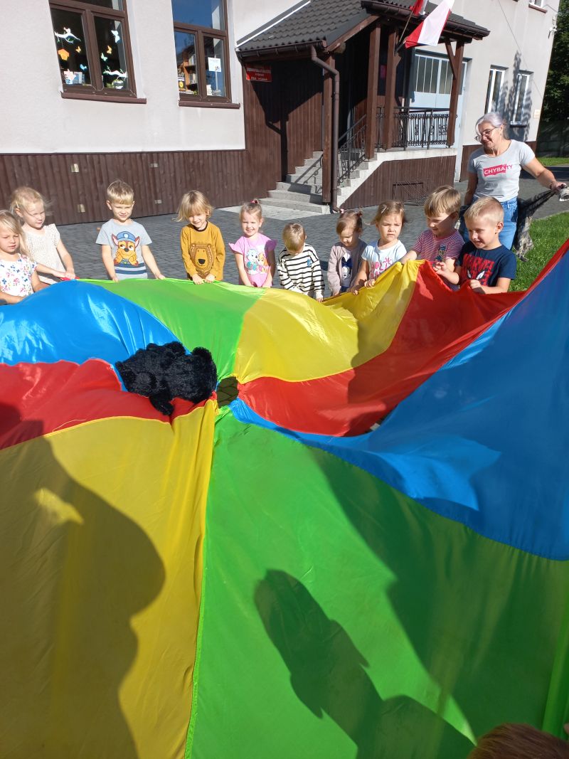 Dzieci bawią się kolorową chustą podrzucając w niej pluszowego misia