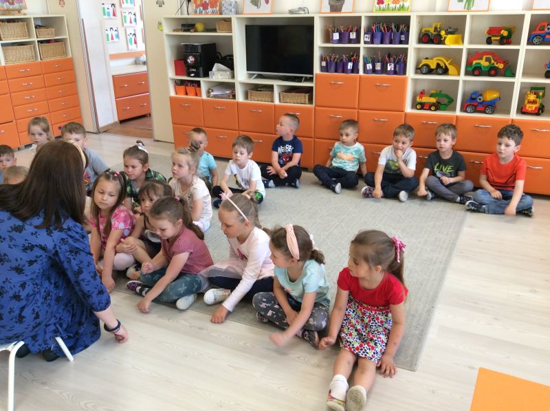 Dzieci w przedszkolu siedzą na dywanie i słuchają czytanej im opowieści