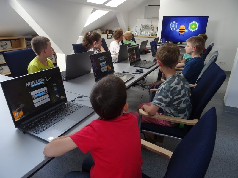 Dzieci siedzą przy stolikach i pracują na komputerach