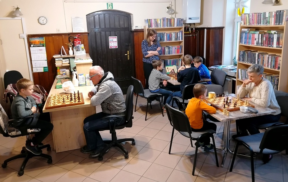Czytelnicy rozgrywają przy stolikach partie szachowe.