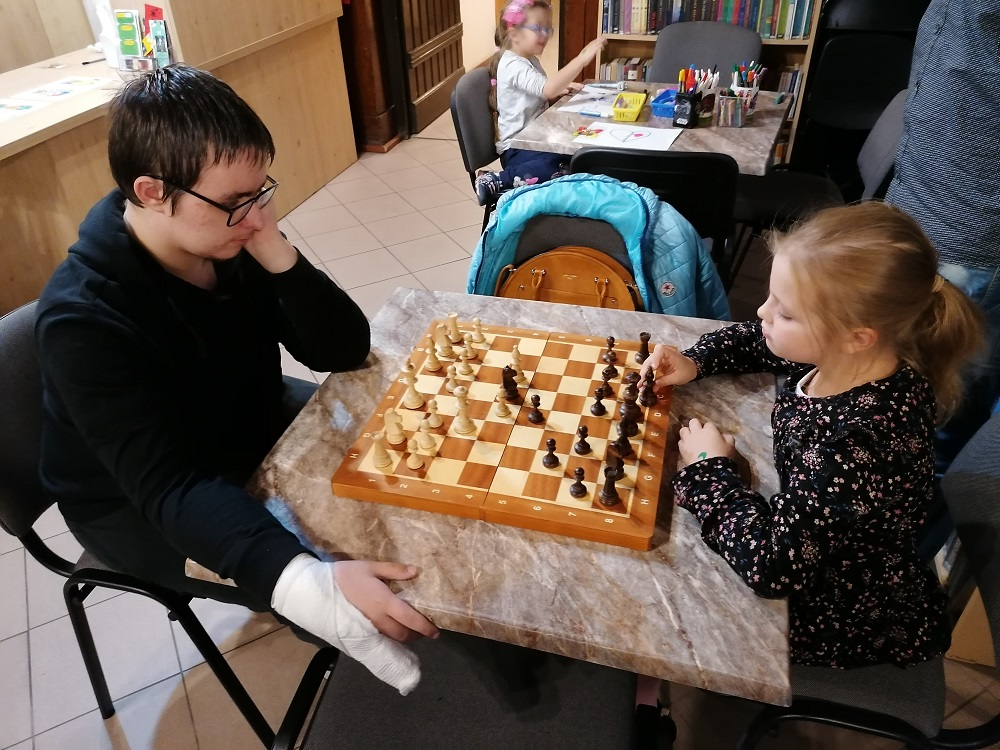 Przy stoliku chłopak z dziewczynką grają w szachy.