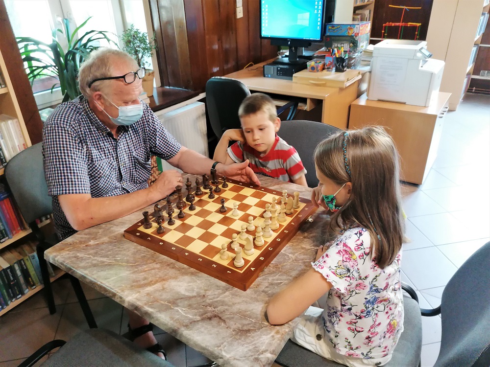 Przy szachownicy instruktor i dwoje dzieci ćwiczą grę w szachy