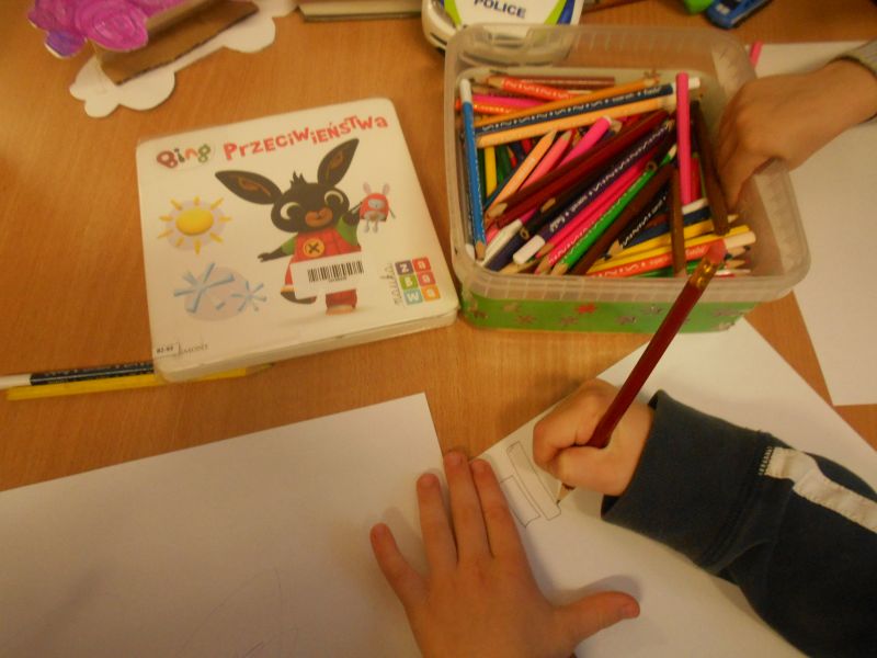 Dzieci z pomocą opiekunów rysują na kartce kredkami różne przeciwieństwa