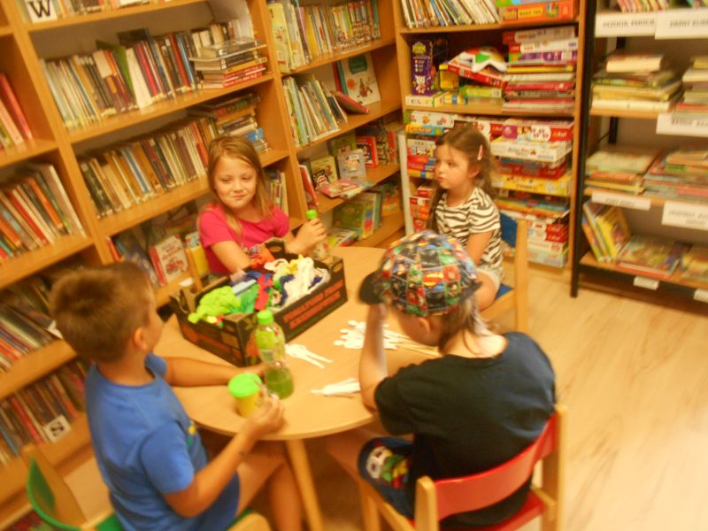 Uczestnicy zajęć siedzą przy stoliku i tworzą własne prace (dwie dziewczynki i 2 chłopców)