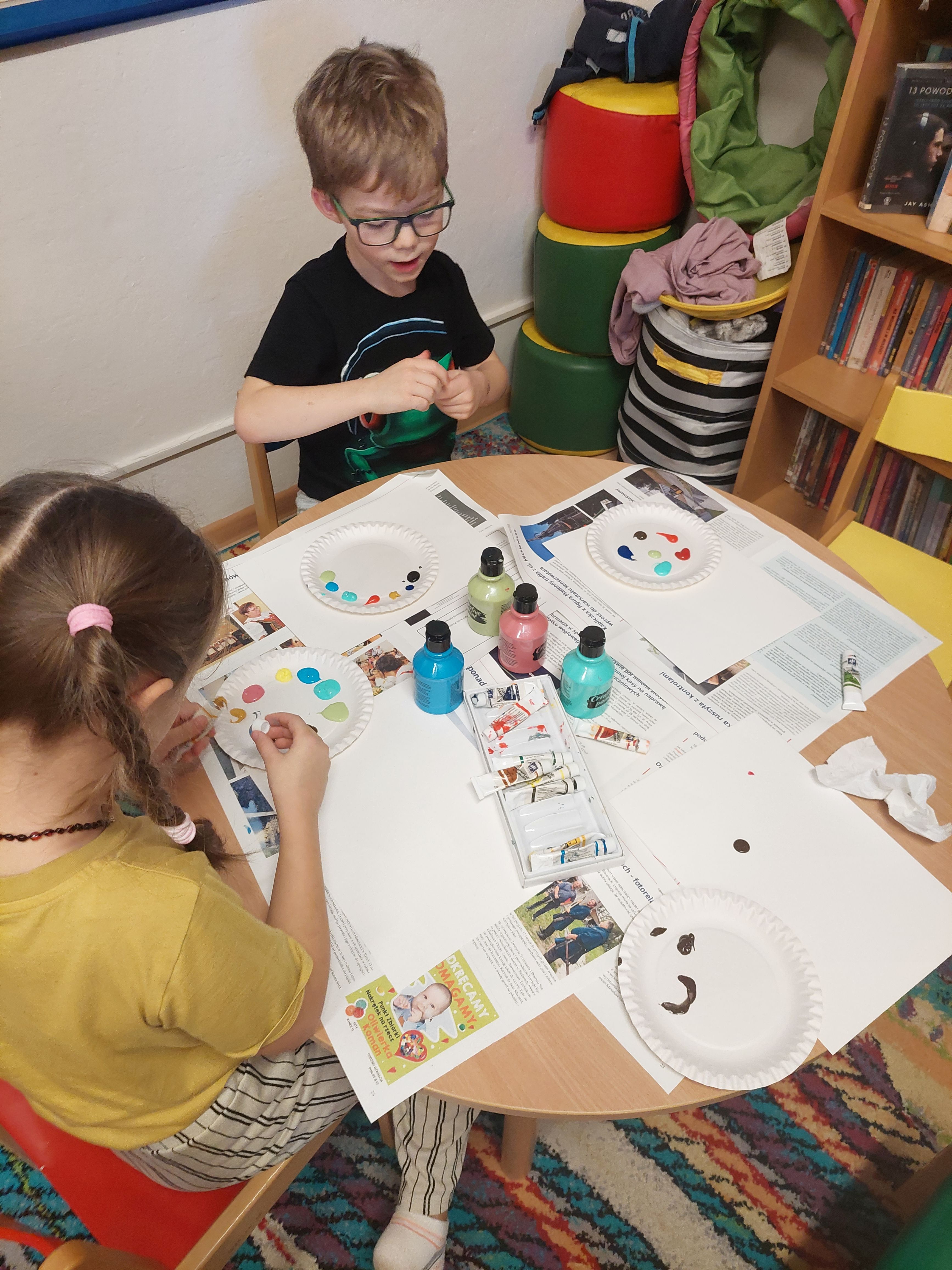 Chłopczyk i dziewczynka malują swoje obrazy przy pomocy odcisków palców  