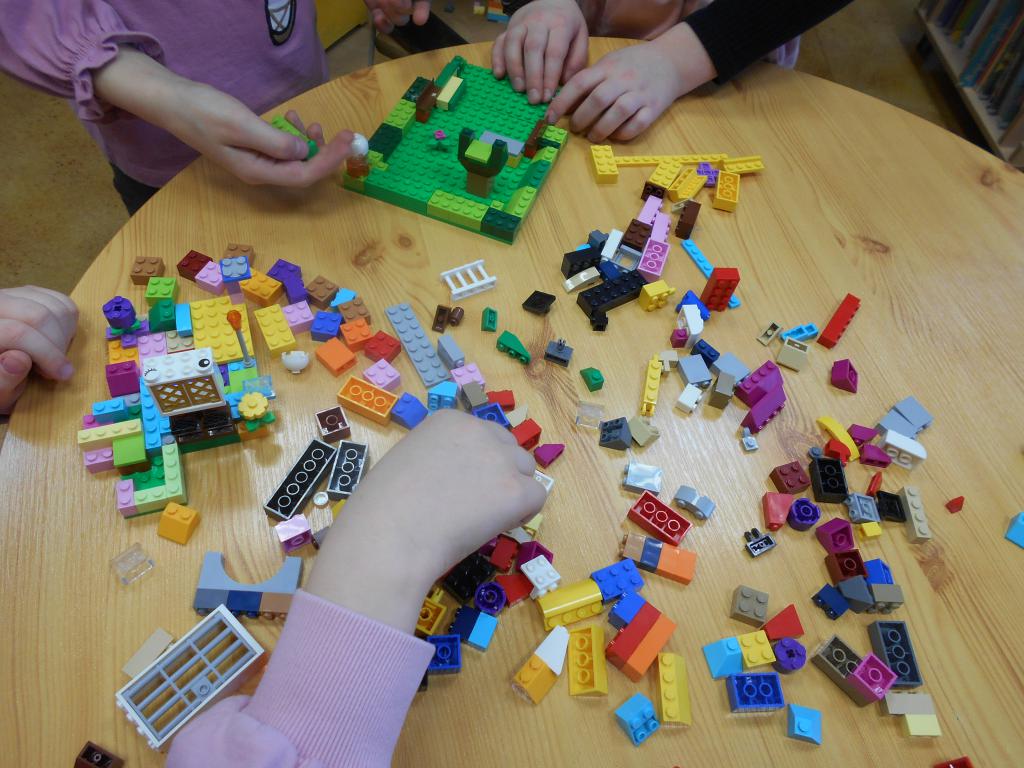 Dzieci układają z klocków LEGO rozsypanych na stoliku