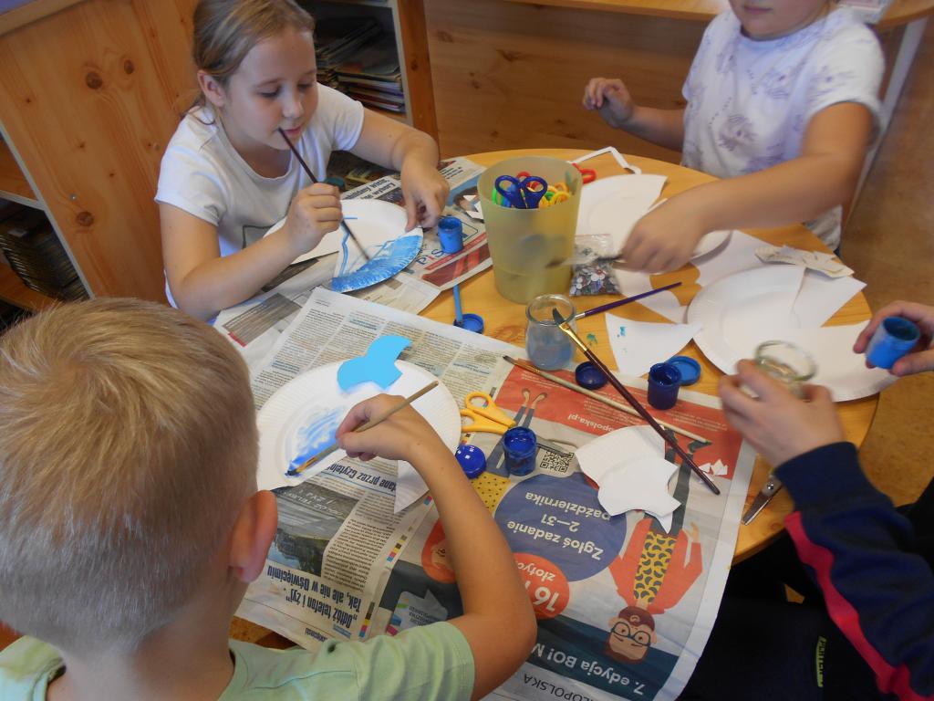 Dzieci na zajęciach plastycznych w bibliotece malują farbami talerzyki papierowe