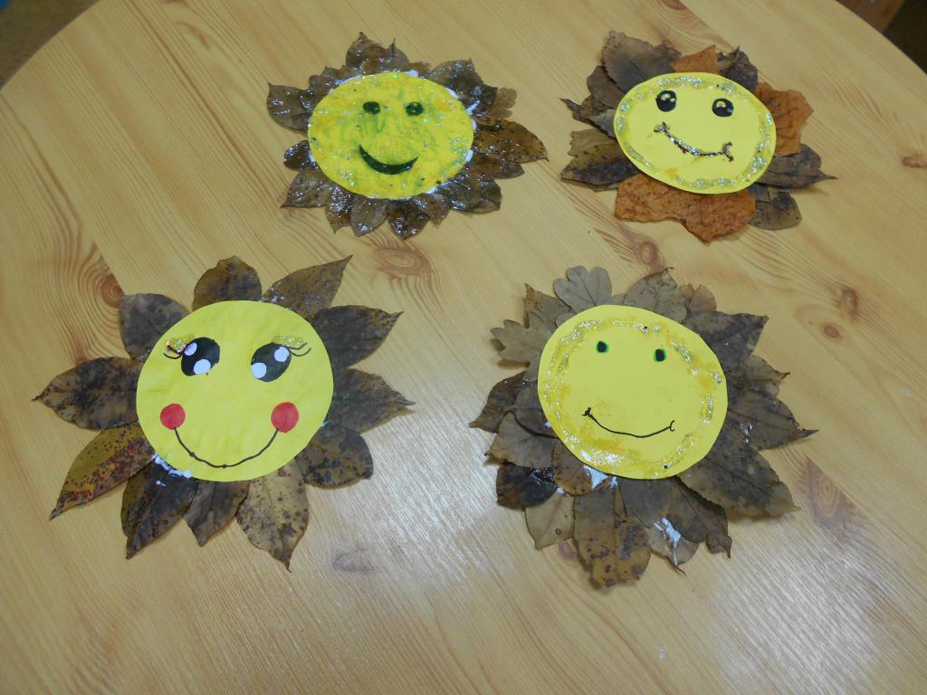 Cztery słońca z jesiennych liści wykonane na zajęciach ułożone obok siebie na stoliku